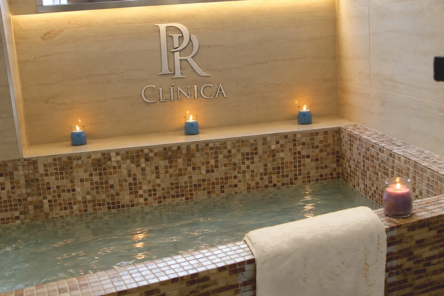 Bañera del spa con velas encendidas bajo el cartel PR Clínica