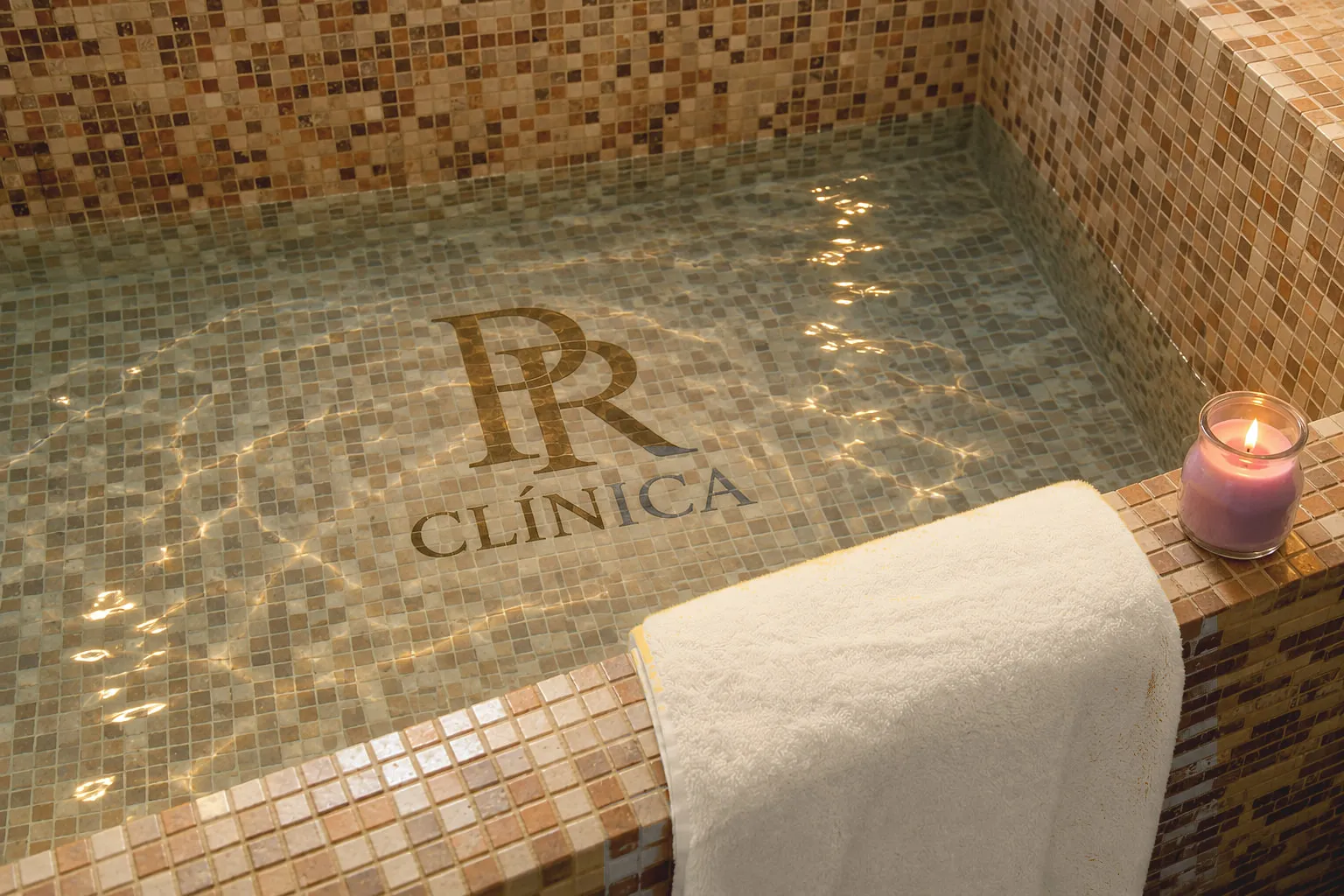 El monograma PR Clínica bajo el agua del spa, junto a una vela y una toalla de lino